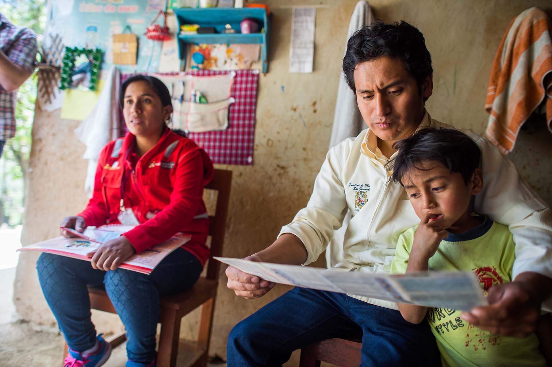Picture of health care workers review the growth chart of a child while speaking to a mother during a home visit. (Sogobamba, Peru) P