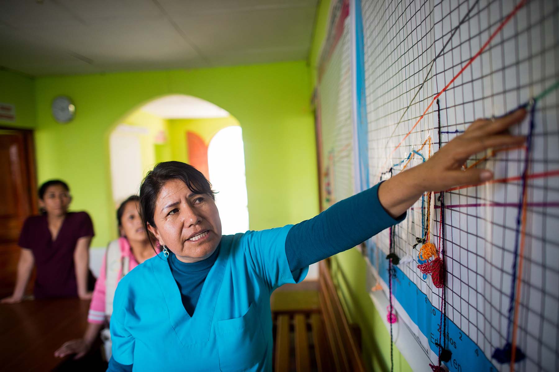 Picture of a health care worker explains a children's growth chart at a local maternal and child community center where health workers track interventions and weight of each child under 3. (Sogobamba, Peru)