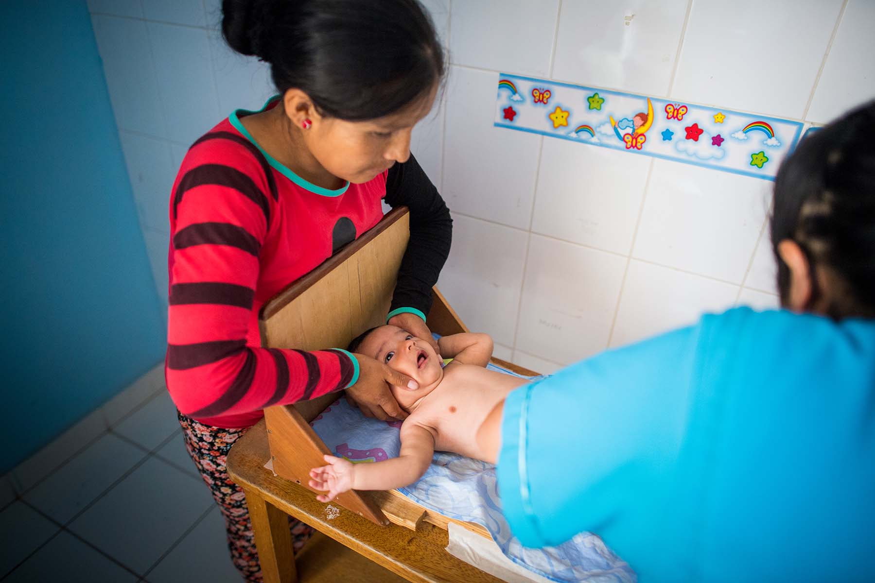 Picture of a mother holds her infant son's head during a height measurement at a local health clinic. (Potracancha, Peru)